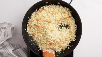 A black skillet with cauliflower rice cooking with carrots.