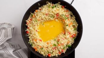 Riced cauliflower and vegetables surrounds a well of beaten eggs.
