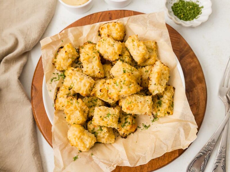Cauliflower tater tots in a bowl next to chopped parsley and some forks.