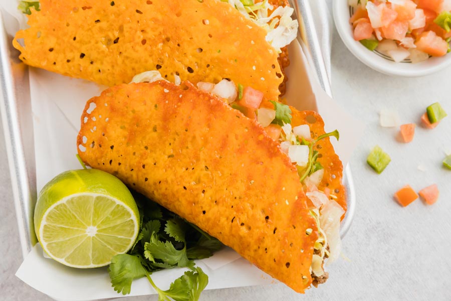 Cheese taco shells fill taco meat and pico de gallo on a tray with a lime slice.