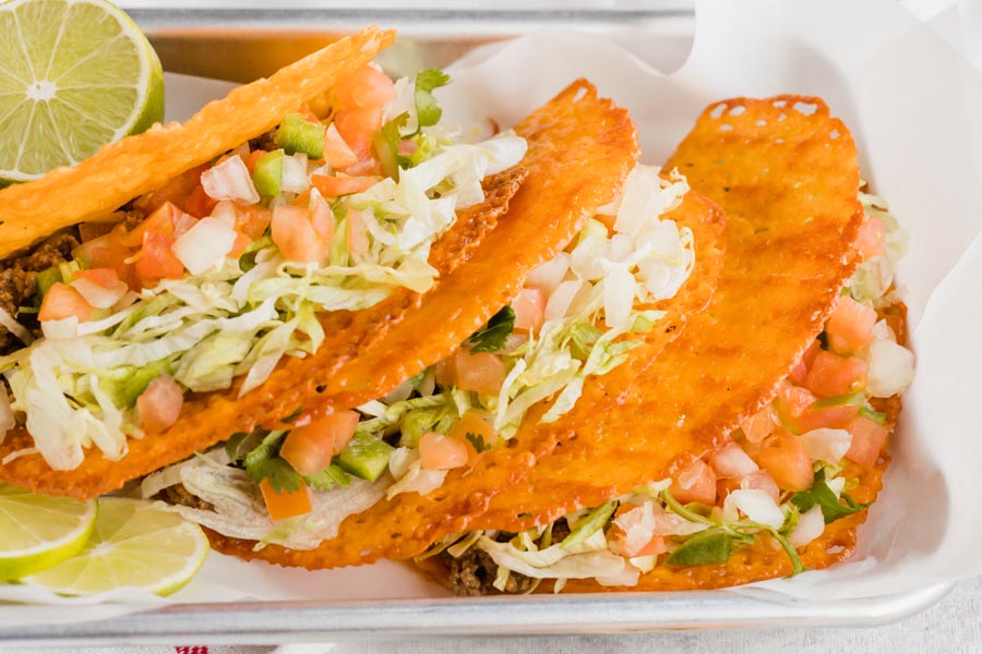 Hard shell tacos made out of cheddar cheese and filled with taco fixings on a tray with slices of lime nearby.