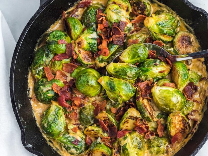 Creamy brussels sprouts casserole topped with bacon in a cast iron skillet.