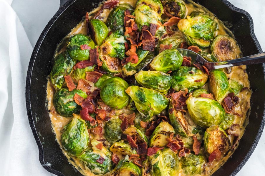 Creamy brussels sprouts casserole topped with bacon in a cast iron skillet.
