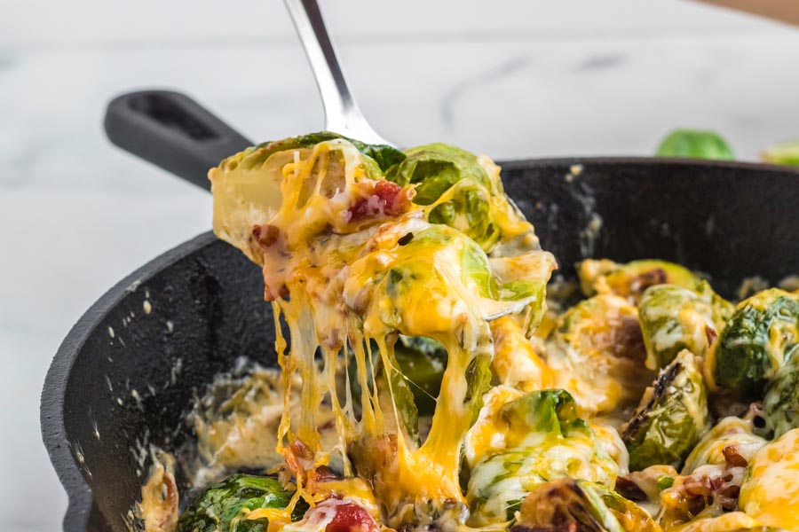 Cheesy brussels spouts pulled out of the skillet with a spoon.