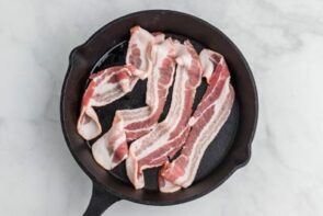 Four strips of bacon in a cast iron skillet.