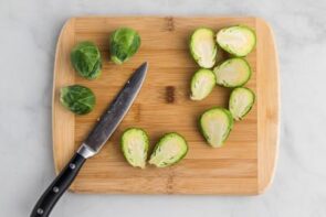 Brussels sprouts sliced in half on a cutting board with a knife near by.