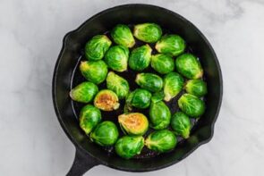 Bright green brussel sprouts frying in a skillet with two flipped over to show the crispy edges.