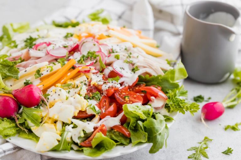 A fresh salad with lettuce, egg, tomato, cheese and radish with ranch dressing nearby.
