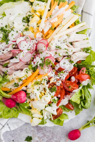 Top down view of a large chef salad filled with fresh veggies, meat and cheese.