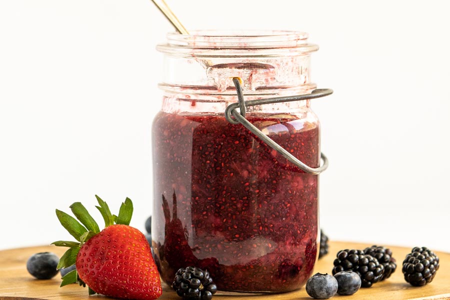 a jar of berry jam next to blueberries and strawberry