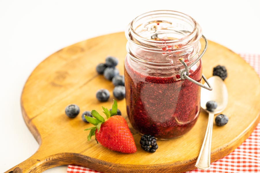 a jam jar on a wooden board with berries scattered around