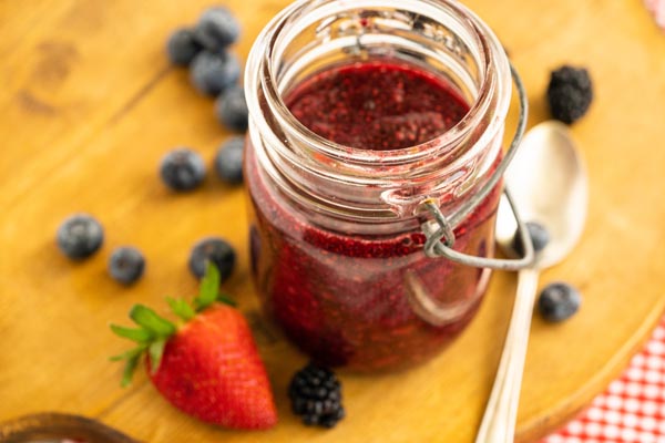 a jar with chia jam inside next to a handful of berries