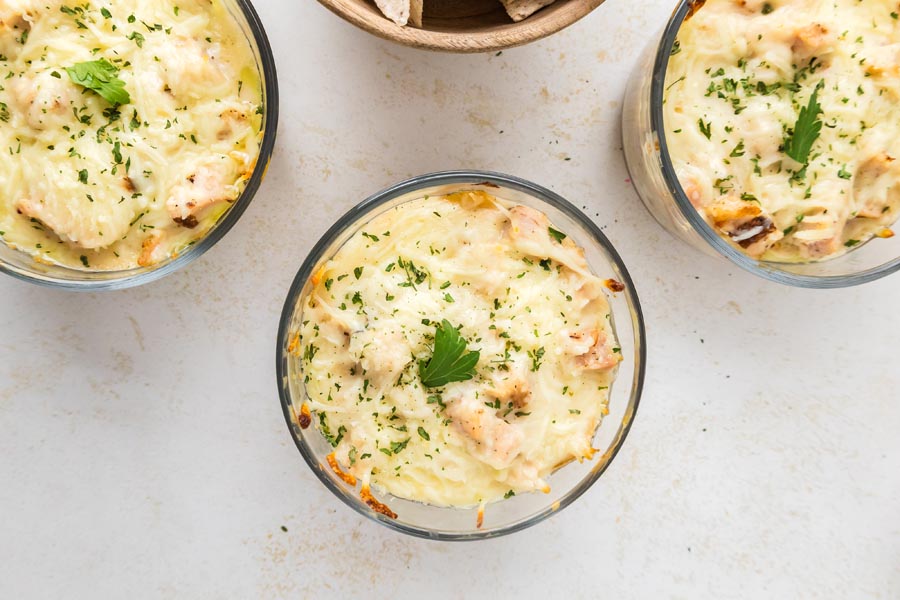Overhead view of baked chicken Alfredo lasagna bowls topped with melted cheese and parsley.