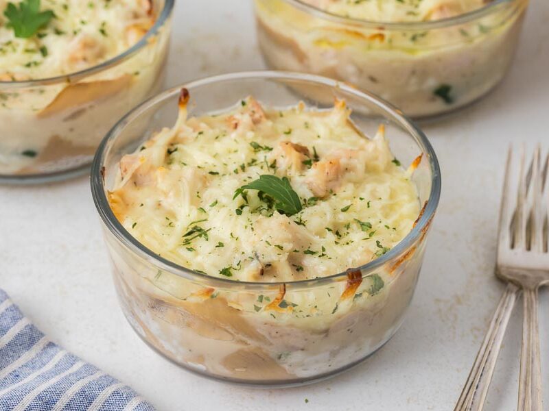 A close-up of a baked lasagna bowl with golden edges and fresh parsley garnish.