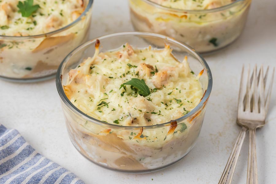 A close-up of a baked lasagna bowl with golden edges and fresh parsley garnish.