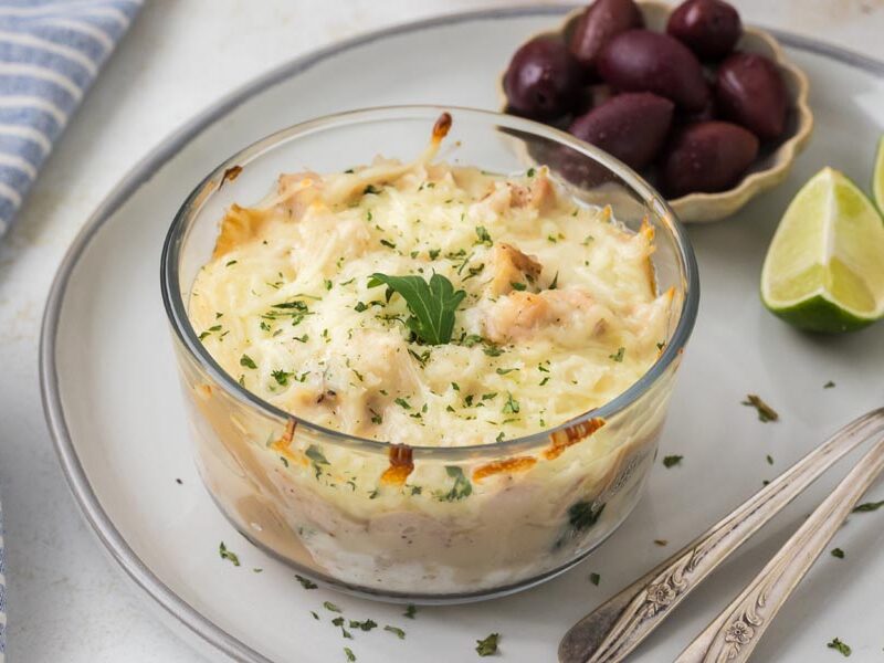 Chicken Alfredo lasagna bowl served on a plate with kalamata olives and lime wedges.