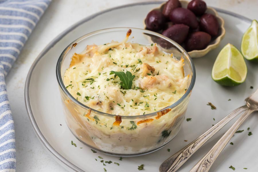 Chicken Alfredo lasagna bowl served on a plate with kalamata olives and lime wedges.