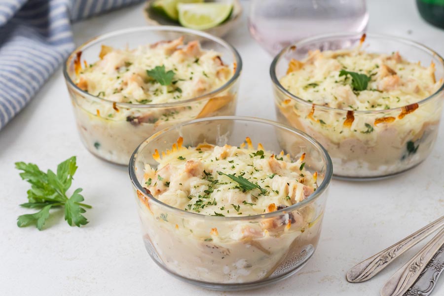 Three baked chicken Alfredo lasagna bowls arranged on a table with fresh parsley.