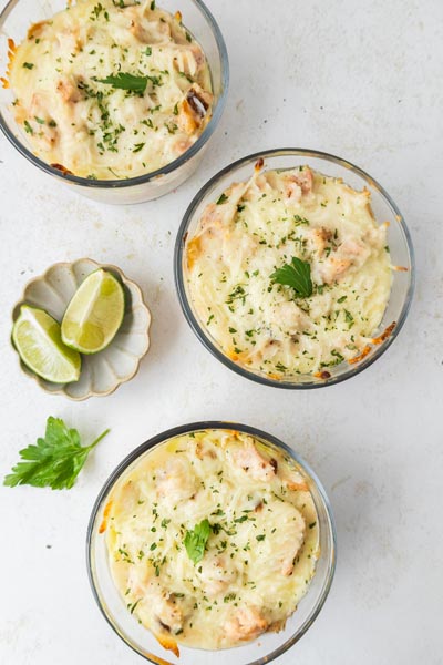 Overhead view of three cheesy Alfredo lasagna bowls with parsley and lime on the side.