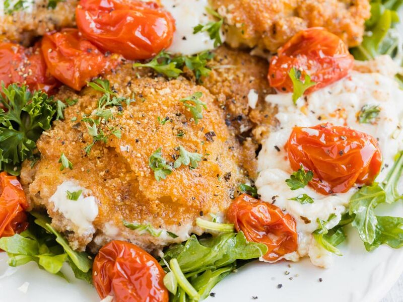 Crispy chicken topped with pepper and parsley next to melted burrata cheese and tomatoes.
