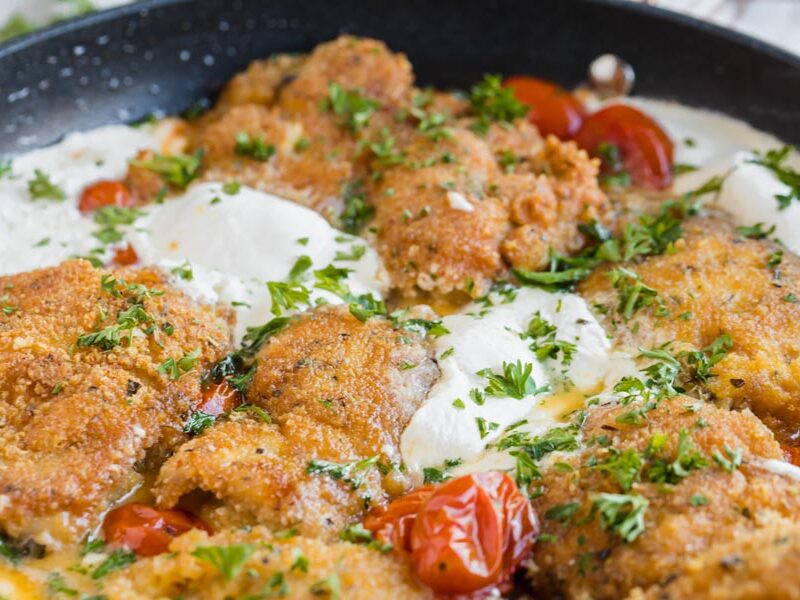 White melted burrata oozing out in a skillet next to crispy chicken.