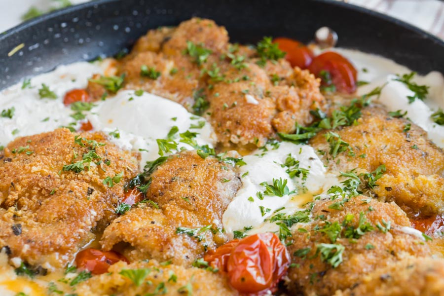 White melted burrata oozing out in a skillet next to crispy chicken.