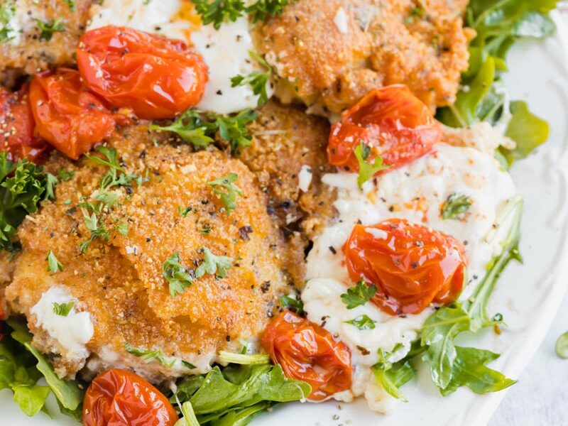 Panko crusted chicken thighs sits next to burst tomatoes and creamy burrata cheese.