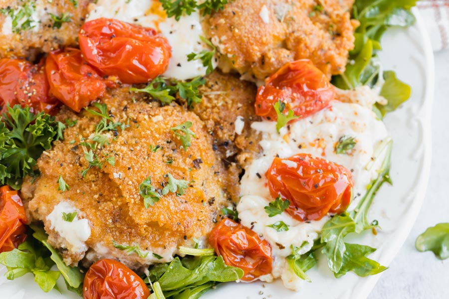 Panko crusted chicken thighs sits next to burst tomatoes and creamy burrata cheese.