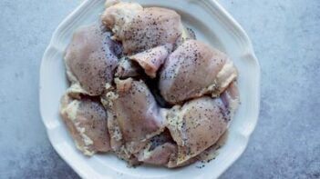 A plate of chicken thighs seasoned with salt and pepper.