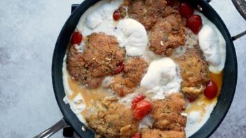A skillet with melted burrata cheese ozzing around crispy coated chicken.