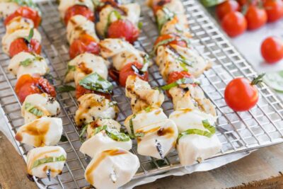 four chicken and tomato kebabs on a rack with mozzarella cheese balls at the end of the skewere