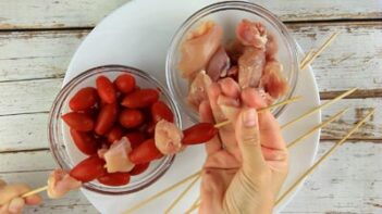 threading a chunk of chicken into a skewer with grape tomatoes