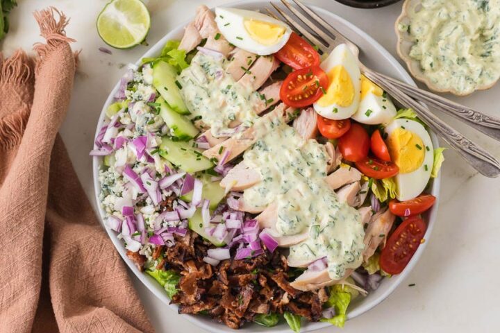 Chicken cobb salad topped with grilled chicken, bacon, eggs, cucumbers, tomatoes, red onion, blue cheese, and creamy herb dressing.