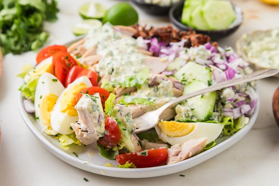 Fork lifting a bite of chicken cobb salad with chicken, egg, lettuce, tomato, and creamy dressing.