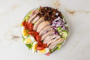 Cobb salad with chicken, bacon, eggs, tomatoes, cucumber and red onion.