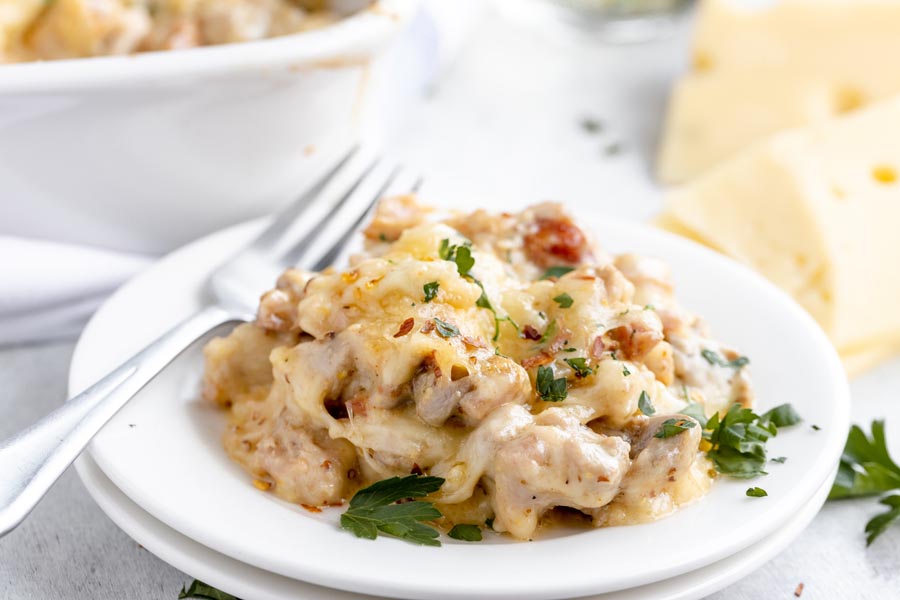 cheesy cordon bleu casserole on a plate, stacked on another plate with parsley on tp and a fork on the plate