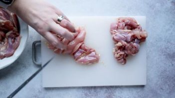 slicing chicken thighs on a white cutting board with a knife