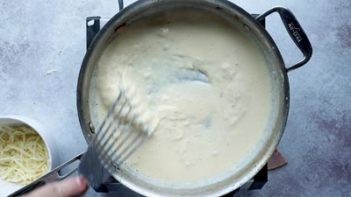 stirring a white wine cheese sauce in a skillet with a metal spatula