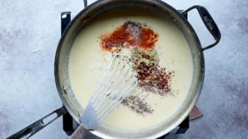a skillet with a creamy cheese sauce in it and dijon, red pepper flakes and cayene sprinkled in