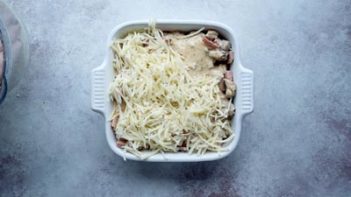 looking down onto a white square baking dish with a casserole inside and topped with shredded white cheese