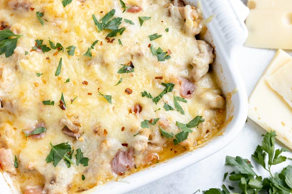 chicken cordon bleu casserole in a white baking dish next to swiss cheese