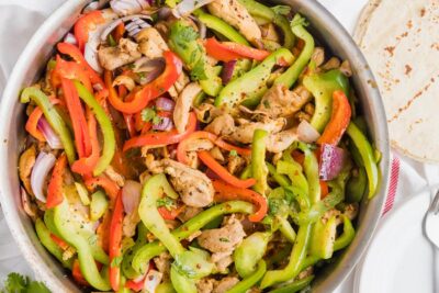 A skillet filled with colorful red and green sliced bell peppers, red onion and slices of cooked chicken.