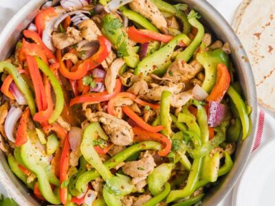 Chicken fajitas with red and green bell peppers and red onion in a skillet.