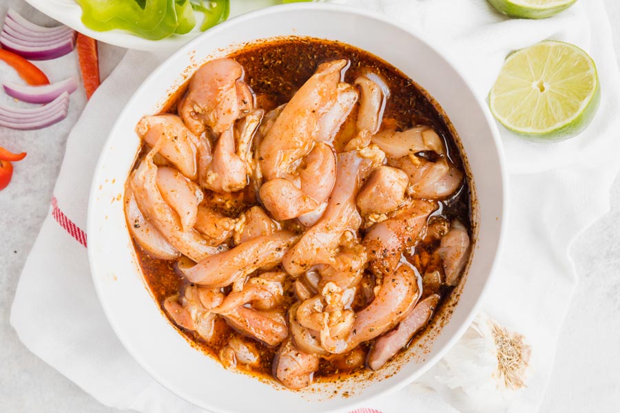 Sliced chicken thighs marinade in a bowl with slice of lime nearby.