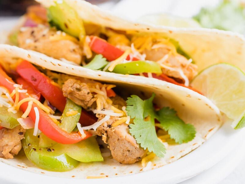 Two chicken fajitas wrapped in a flour tortilla on a plate.