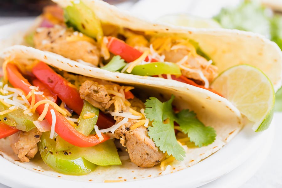 Two chicken fajitas wrapped in a flour tortilla on a plate.