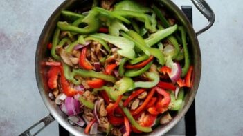 Raw bell pepper and purple onion in a skillet with cooked chicken.
