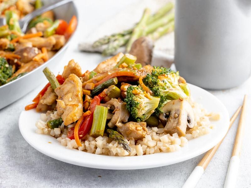 Chicken and vegetable stir-fry over cauliflower rice with a skillet in the background.