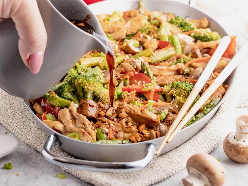 pouring sauce into a skillet with cooked stir fry vegetables