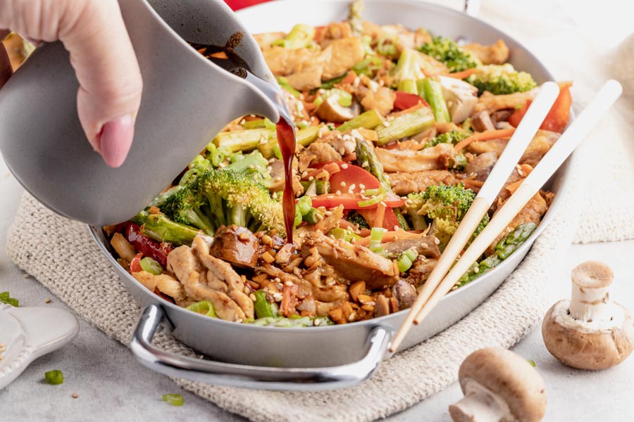 pouring sauce into a skillet with cooked stir fry vegetables